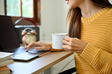 cropped image, A female remote working in the coffee shop, using laptop and sipping coffee.