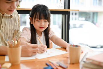 Smiling and cute young Asian girl having a great time with her art teacher, practice drawing