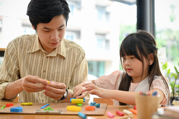Pretty Asian girl concentrating sculpting play dough, making a colorful clay with her art teacher