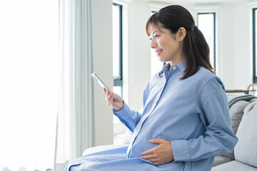 室内で微笑みながら携帯を見る日本人妊婦