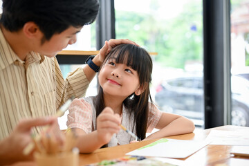 Happy proud Asian dad and daughter having fun together, drawing and painting watercolor
