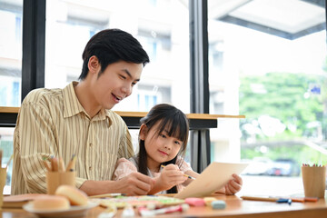 Happy young Asian daughter is enjoying a painting workshop with her father.