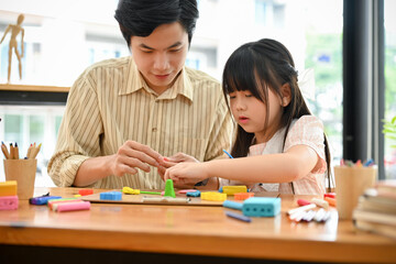 Smiling Asian male art teacher and a young girl moulding colorful clay or plasticine together