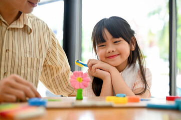 Lovely young Asian girl admiring a cute flowers play dough, having fun time with her dad