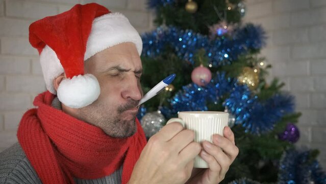 Sick man at Christmas eve. An upset sick man in Santa hat measure his body temperature during quarantined Christmas eve.