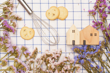 Flat lay of sweets, Danish butter cookie and model house with statice flower on blue gingham cloth