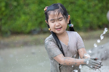 Happy little child girl playing in wet mud puddle during rainy season