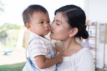Mother kissing on cheek her little son. Happy Asian mum embracing little son and kissing on cheek outdoors
