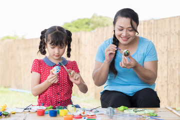 Smiling adult woman and child girl painting eggs with brush and sculpts modeling clay multi-colored...