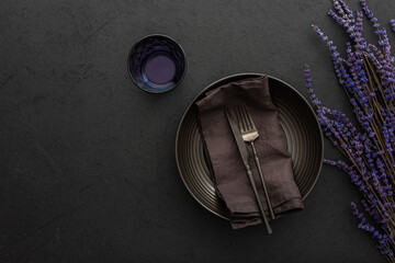 Fototapeta na wymiar Table setting, empty plate with napkin and cutlery on a black background, top view of the served table decorated dry lavender flowers