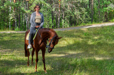 Woman in casual clothes rides a horse in early spring