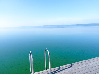 Fototapeta na wymiar Photo blooming green lake with pier. Handrails for launching into the water