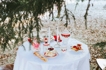 table covered with white tablecloth for breakfast outside in winter, tea, croissants and cakes, a romantic picnic date