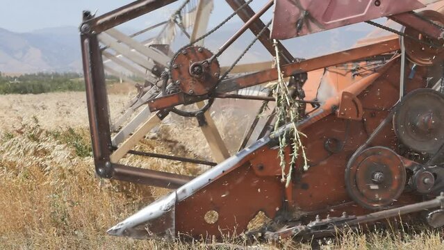 old used combine harvester harvesting grain moving across a field in a mountainous area on a sunny hot day. Harvesting cereals in poor countries. Grain Crisis