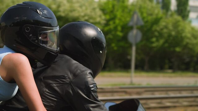 Happy couple in protective helmets rides contemporary motorcycle spending time together along city street on sunny day slow motion closeup