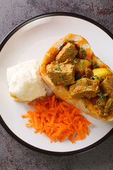 Durban Bunny Chow or a quarter mutton bunny consisting of a section of a loaf of bread hollowed out and filled with mutton curry and gravy closeup on plate on the table. Vertical top view from above