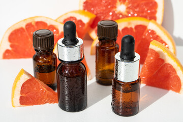 Bottles of grapefruit essential oil on a white background. Bottled essential oil, grapefruits in the background. Bottles of perfume oil and grapefruit. Selective focus. 