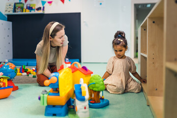 Playtime at nursery school. Toddler girl with a teacher sitting on the floor and playing with...
