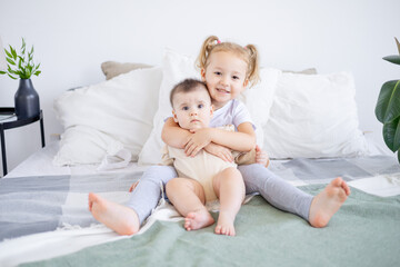the older sister holds and hugs the baby at home on the bed, the love and friendship of the sisters in the family