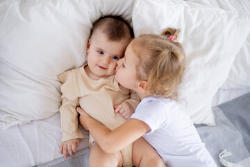 Fototapeta na wymiar older sister baby kisses and hugs baby at home on the bed, love and friendship of sisters in the family