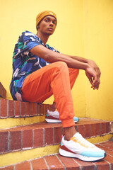 Black man, fashion and street style clothes on cool, trend or attitude model on steps by city wall background on building. Portrait of serious student sitting on stairs in urban punk clothing outdoor - obrazy, fototapety, plakaty