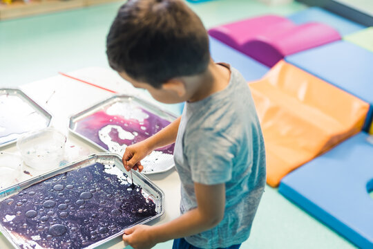 Sensory play for early brain development at nursery school. Toddler boy milk painting with his fingers, using nontoxic food coloring for colors, milk and trays. Creative kids activity for fine motor