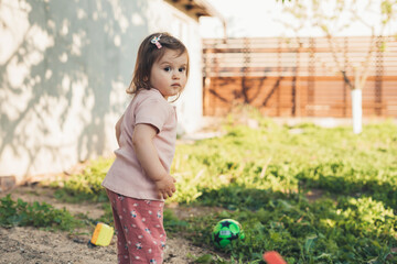 Cheerful baby girl standing alone on a playground and playing in the sand on a sunny summer day. Outdoor leisure activity. Learn through play