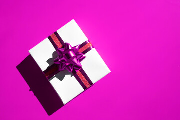 Gift box with ribbons and a bow on a bright purple background. Top view, place for text.