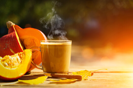 Pumpkin latte coffee with spices and cinnamon. Autumn hot drink on a rustic wooden table decorated with yellow leaves and pumpkin under the sun. Cosiness, halloween, warmth concept. 