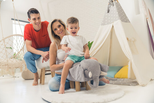 Toys for little kids. Living room interior. European cute family of three - two parents and one baby boy - playing together in the boho-styled living room. Fun elephant toy. High quality photo