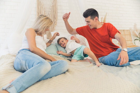 Quality leisure time with family. Two adult European married people lying on the bed and tickling their beloved four-year-old son. Casual clothing. High quality photo
