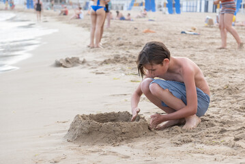 Cute boy on the beach plays with sand. Relax travel concept. Sea holidays, copy space