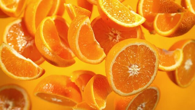 Super Slow Motion Shot of Flying Fresh Orange Slices Towards Camera on Orange Background at 1000fps.