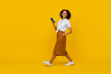 Full size profile photo of cheerful pretty person walk hold telephone isolated on yellow color background