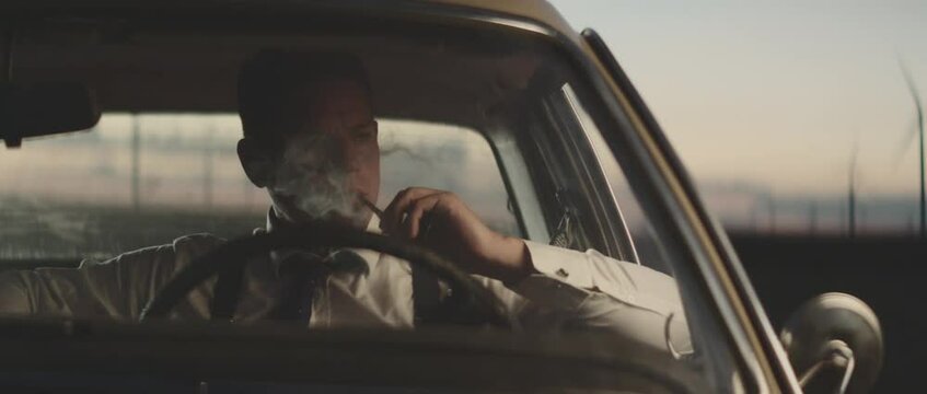 Serious adult man sitting in car and smoking pipe. Retro style detective using deduction for solving challenging cases.