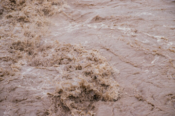 Muddy river water. Spring flood. Dirty muddy water with a whirlpool and white foam close-up.A mountain river or stream raging during a flash flood.