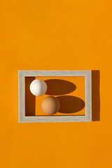 Two vertically standing chicken eggs in a rectangular frame on an orange background