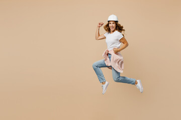 Full length fun young employee laborer handyman woman in white t-shirt helmet jump do winner gesture isolated on plain beige background Instruments accessories for renovation room Repair home concept