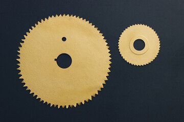 Two circular saw blades with teeth painted in gold on a black background