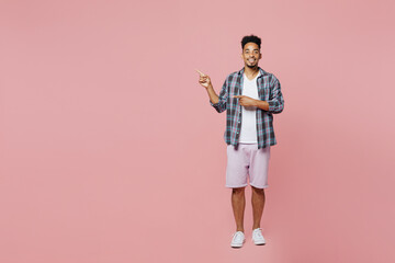 Fototapeta premium Full body young smiling man of African American ethnicity 20s wear blue shirt pointing index finger aside indicate on workspace area copy space mock up isolated on plain pastel light pink background.
