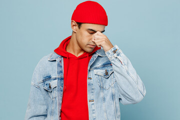 Young sad tired sick ill middle eastern man 20s he wear denim jacket red hat keep eyes closed rub put hand on nose isolated on plain pastel light blue cyan background studio. People lifestyle concept.