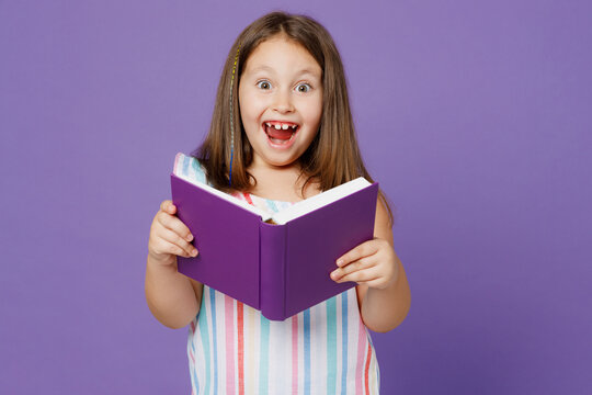 Little surprised happy smart excited kid child girl 5-6 years old wears striped dress read book fairy tale isolated on plain pastel light purple background. Mother's Day love family lifestyle concept.