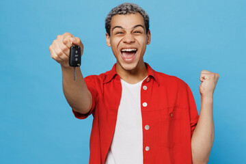 Young overjoyed man of African American ethnicity 20s he wear red shirt hold car key fob keyless system do winner gesture isolated on plain pastel light blue cyan background. People lifestyle concept.