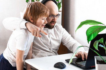 dad and son hugging having fun and playing video game on the computer at home. cheerful family spending time together look at the laptop screen