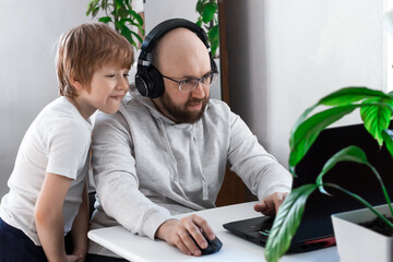 dad and son laughing having fun and playing video game on the computer at home. cheerful family spending time together look at the laptop screen