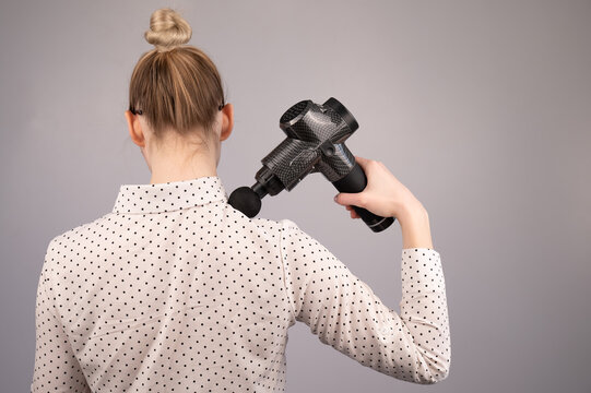 Caucasian business lady makes herself a back massage with a massager gun on a white background.
