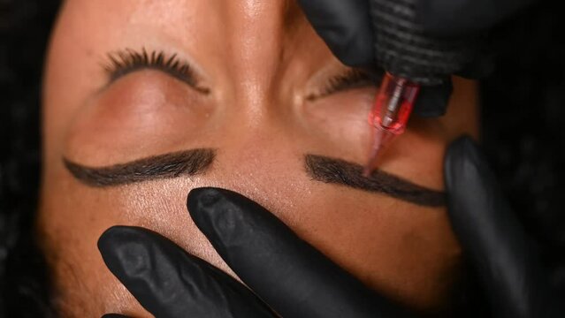 Microblading, permanent makeup or tattooing of eyebrows by professional. A closeup of female eyebrows being painted by semi-permanent makeup.