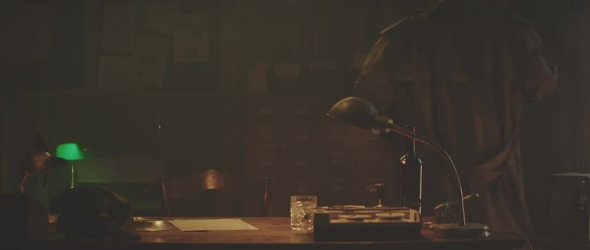Man coming into his office, takes off coat and sitting down at desk. Retro style detective using deduction for solving challenging cases.