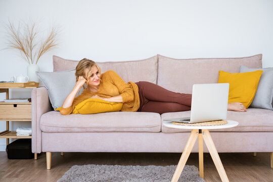 Business freelance woman working on laptops, checking social media, lying on sofa and watching movie while relaxing in living room at home. Lifestyle at home caucasian girl freelancer concept.