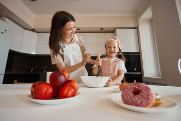 Family in the kitchen. Beautiful mother with her little daughter. A woman in an apron is kneading. Girl learning to cook dough